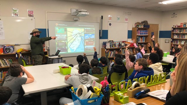 Park Ranger in a classroom pointing towards students with raised hands